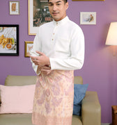 man dressed in a traditional baju melayu set white stands confidently while looking to the camera