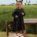 cheerful little girl donning melati print holiday dress, while standing on chair