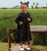 cheerful little girl donning melati print holiday dress, while standing on chair