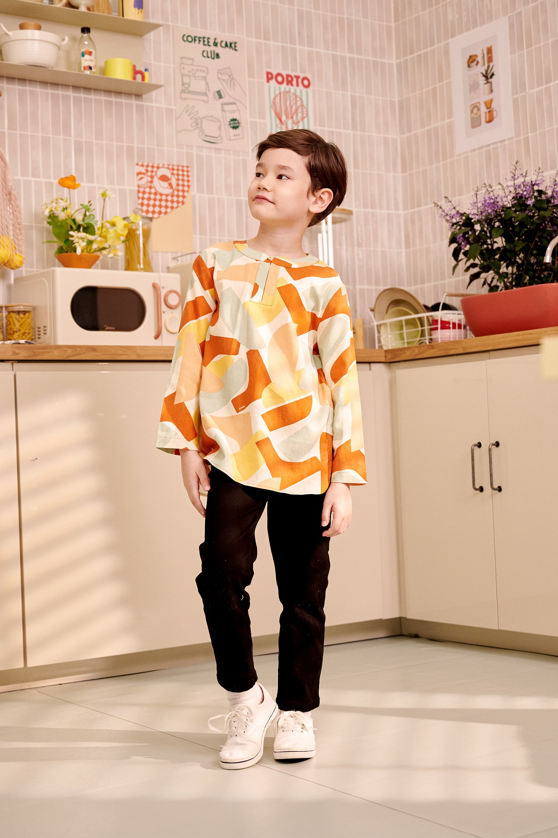 boy staring sideways in marmalade print orange teluk belanga top