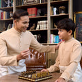 father and son wearing caramel baju melayu set playing chess