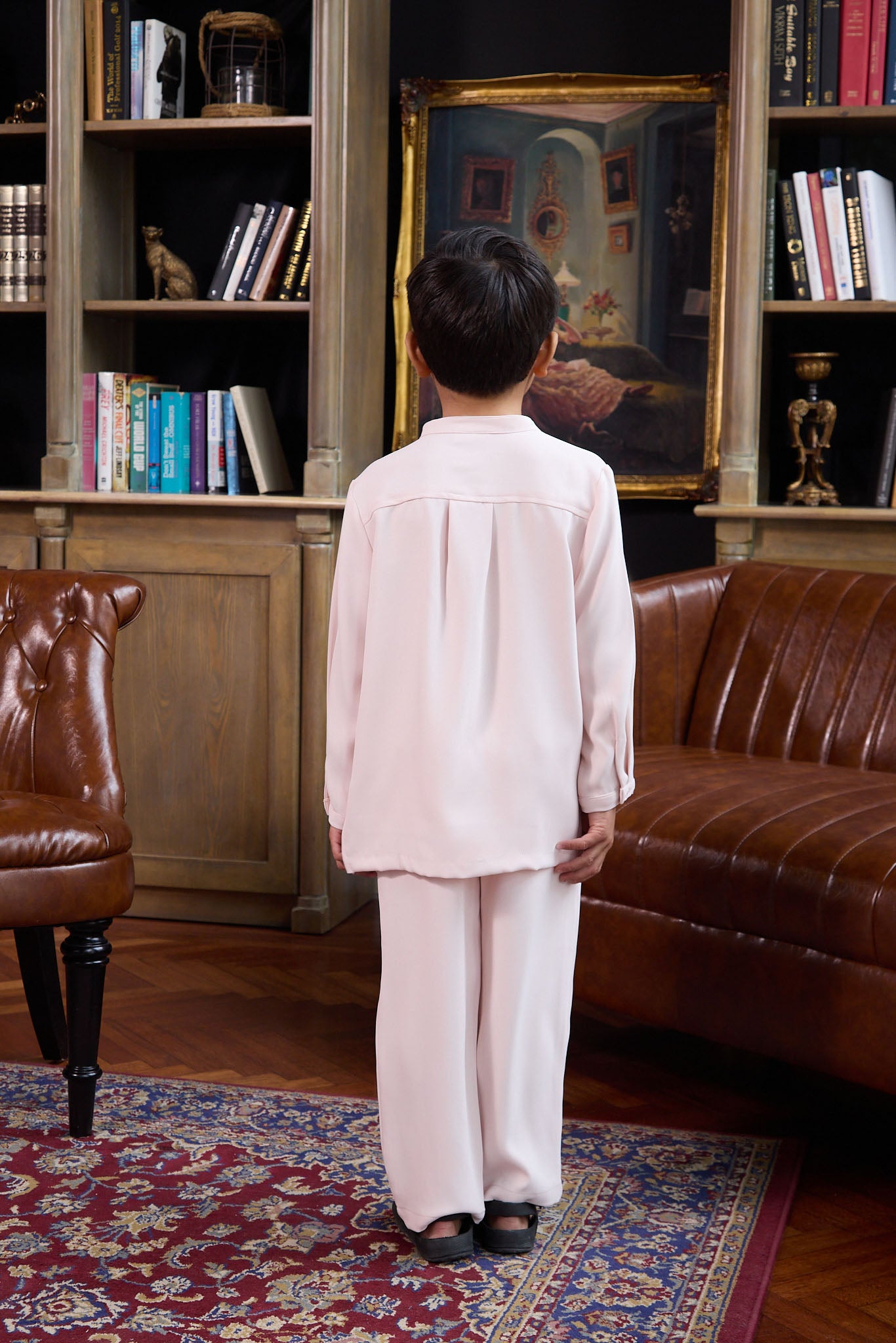 young boy standing backwards posing in boy baju melayu set pink