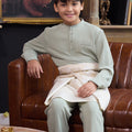 young boy smiling and sitting on chair wearing sage green boy baju melayu set