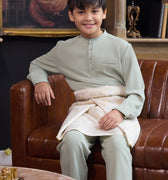 young boy smiling and sitting on chair wearing sage green boy baju melayu set