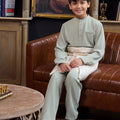 young boy donning boy baju melayu set sage green and sitting on chair