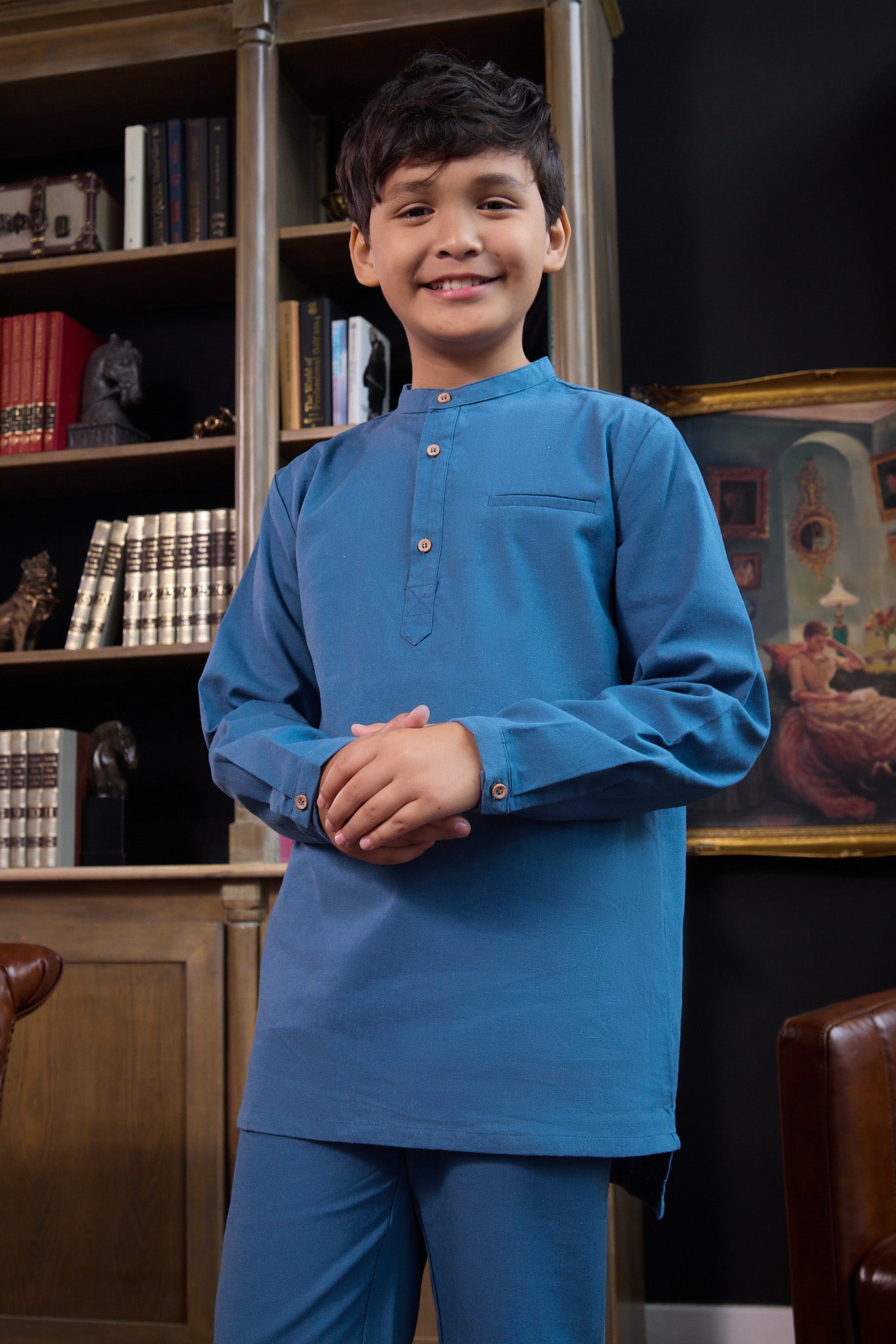 smiling boy with clasped hand posing, wearing steel blue boy baju melayu set