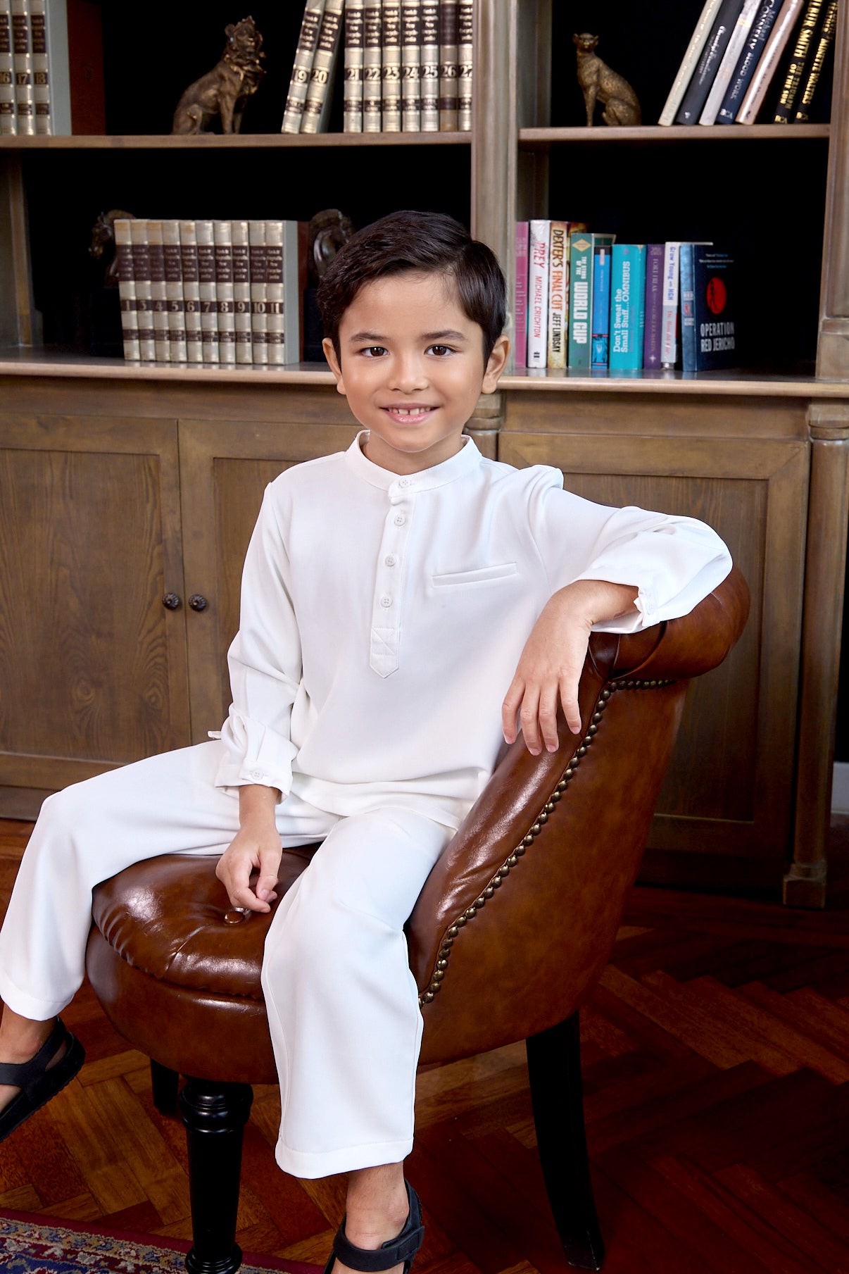 little boy sitting on chair wearing white boy baju melayu set