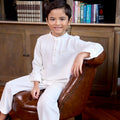 little boy sitting on chair wearing white boy baju melayu set