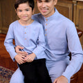 son sitting on father's lap, wearing the warisan raya stone blue matching together