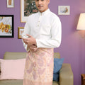 man dressed in a traditional baju melayu set white stands confidently while looking to the camera