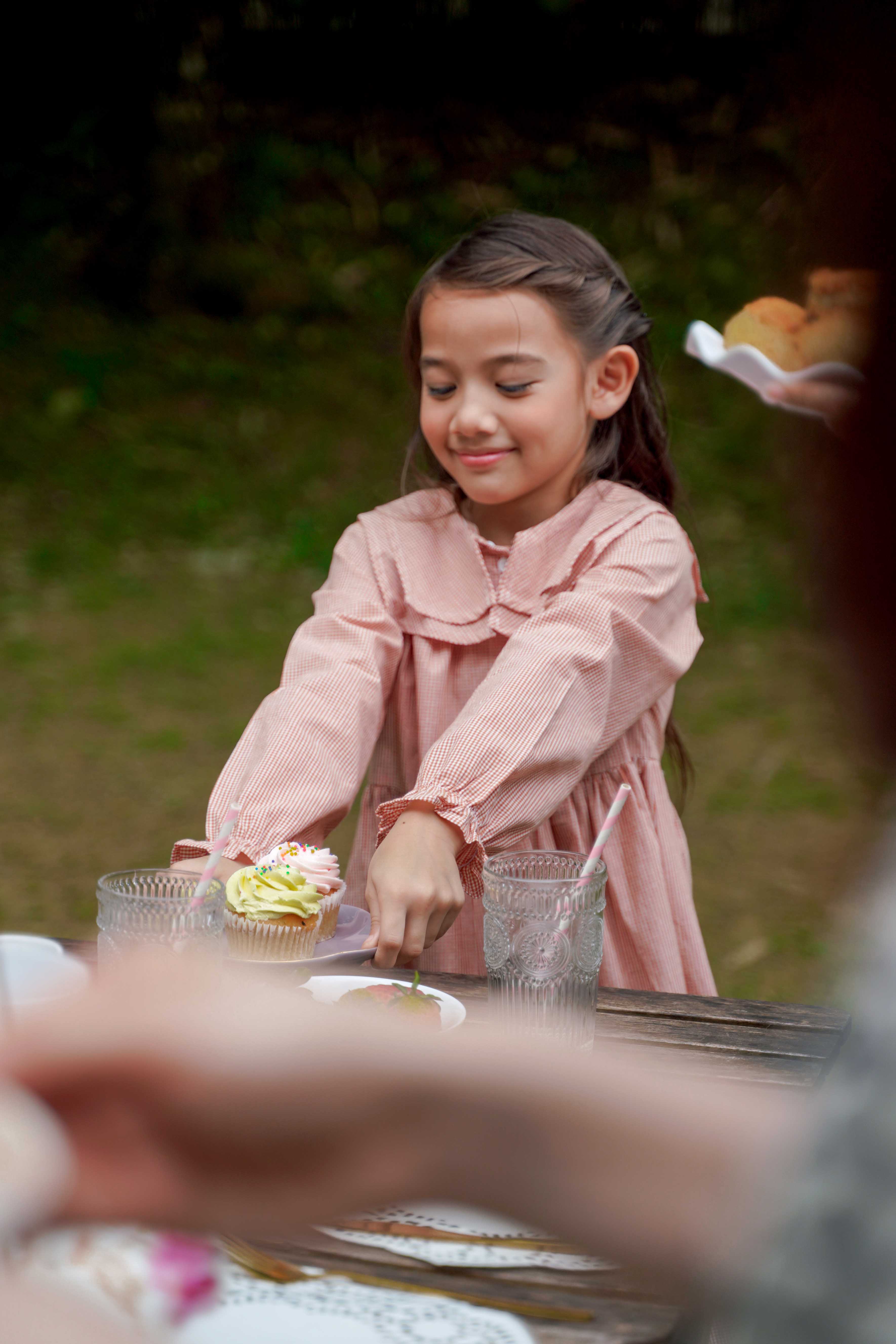 girl in checked red dress serving cupcake